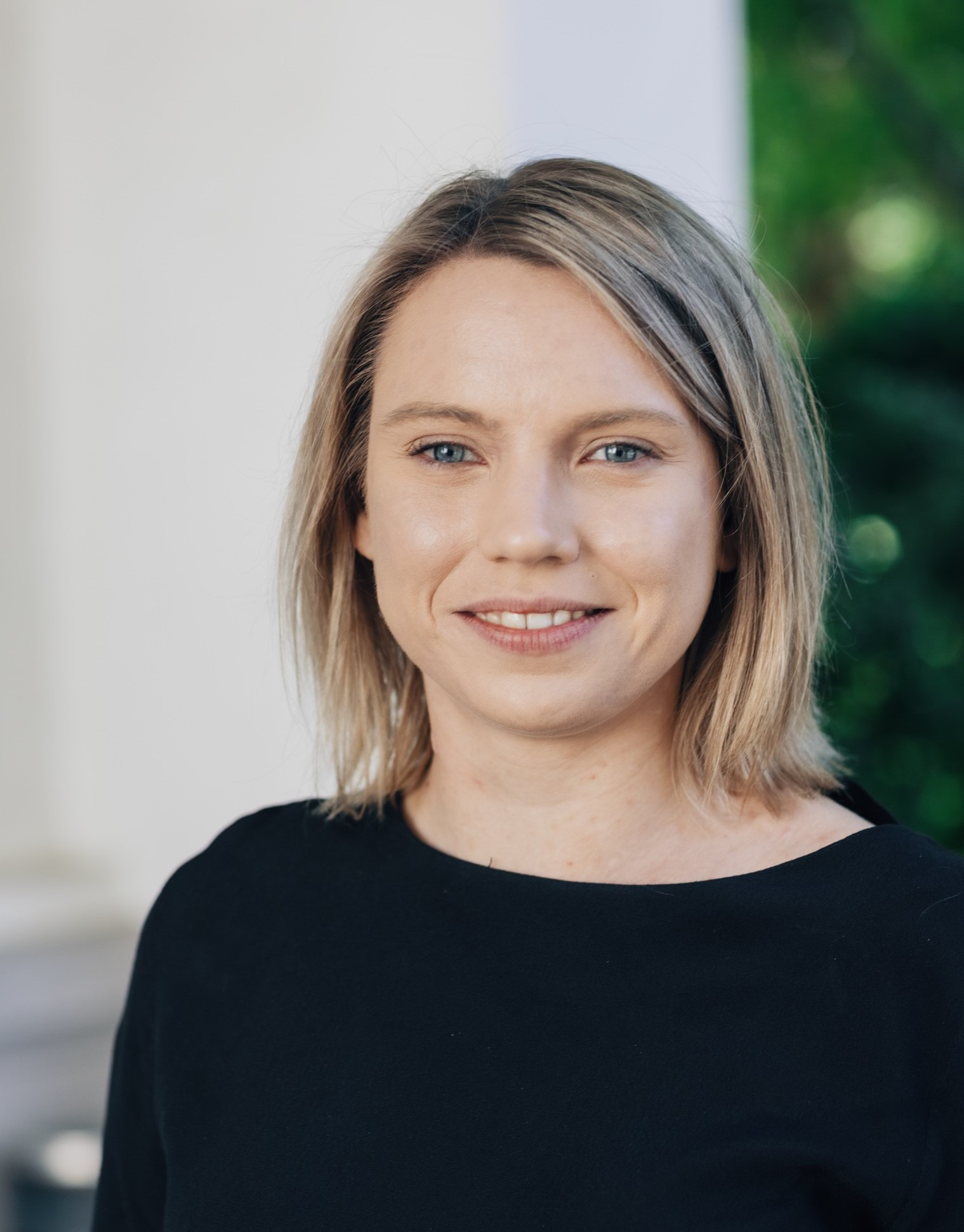 Portrett av Nina Herland utendørs foran hvit vegg.